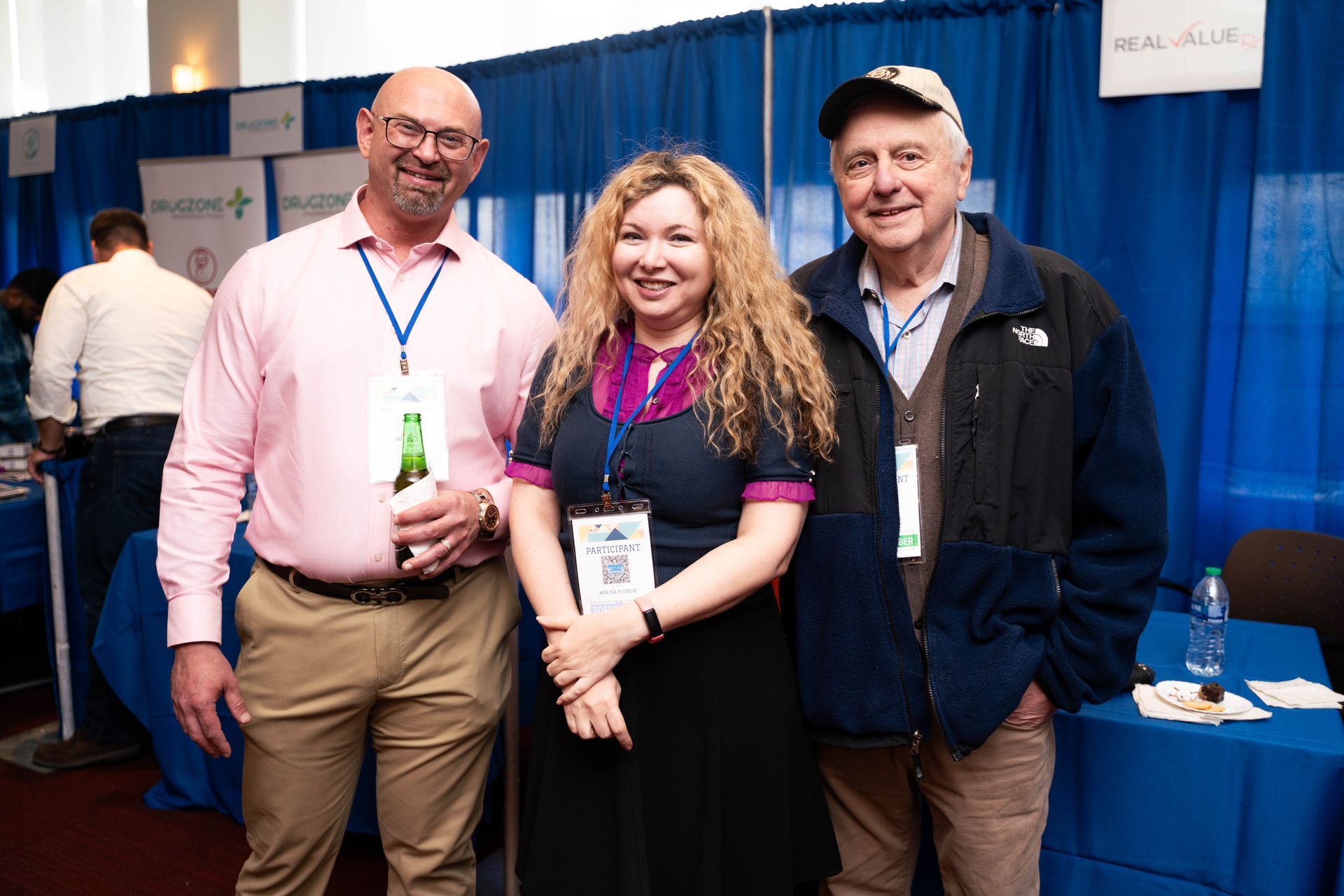 Three attendees smiling in front of the exhibitor booths